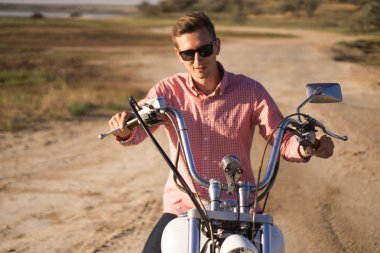 Genç şık motosikletçi gün batımında çöl yolunda onun motosiklet üzerinde oturan