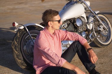 Genç şık motosikletçi gün batımında çöl yolunda onun motosiklet üzerinde oturan