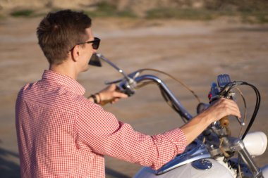 Genç şık motosikletçi gün batımında çöl yolunda onun motosiklet üzerinde oturan