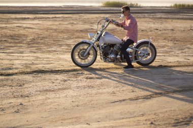 Genç şık motosikletçi gün batımında çöl yolda onun motosiklet sürüş