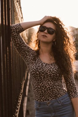 Mutlu kıvırcık genç kadın açık havada gülümseyen ve gün batımında şehir caddesinde yürüyüş 