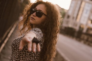 Mutlu kıvırcık genç kadın açık havada gülümseyen ve gün batımında şehir caddesinde yürüyüş 