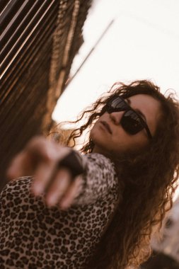 Mutlu kıvırcık genç kadın açık havada gülümseyen ve gün batımında şehir caddesinde yürüyüş 