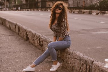 Mutlu kıvırcık genç kadın açık havada gülümseyen ve gün batımında şehir caddesinde yürüyüş 