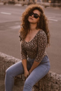 Mutlu kıvırcık genç kadın açık havada gülümseyen ve gün batımında şehir caddesinde yürüyüş 