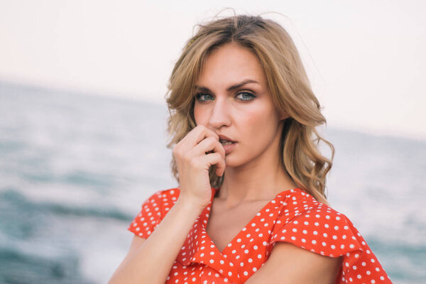 Outdoor fashion portrait of beautiful blonde lady at beach in the red dress on sunset