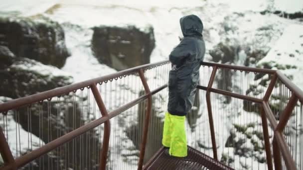 Yeşil pantolonlu genç kadın İzlanda 'da bir köprüde duruyor ve kanyona bakıyor.