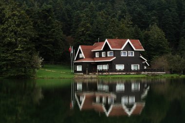 Bolu Golcuk Milli Parkı 'ndaki ormanın içindeki ahşap göl evi, bulutlu gökyüzünde yansıyan gölle birlikte Türkiye..