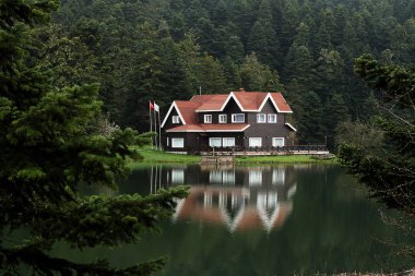 Bolu Golcuk Milli Parkı 'ndaki ormanın içindeki ahşap göl evi, bulutlu gökyüzünde yansıyan gölle birlikte Türkiye..