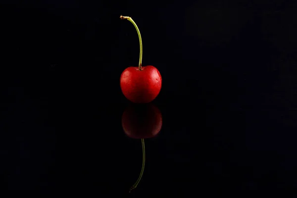 Macro photo of red cherry with water drops on black background. Selective focus. Lights and shadows