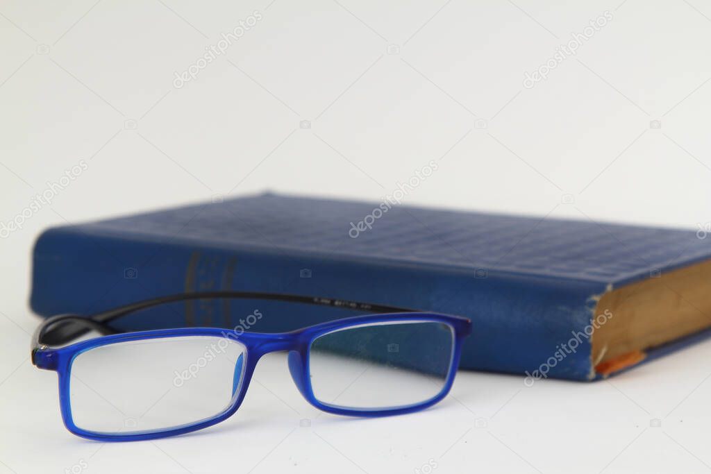 Hardcover beige book and reading glasses on white slate board.