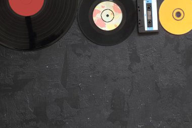 Müzikal depolama cihazları ve kopyalama alanı. Eski ses kasetleri, küçük disk ve beyaz ahşap arka planda metin alanı olan vinil kayıt.