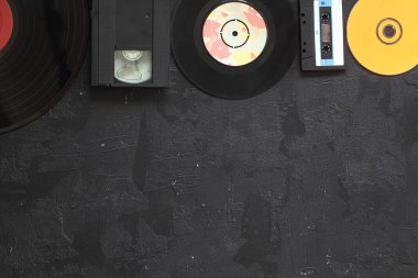 Müzikal depolama cihazları ve kopyalama alanı. Eski ses kasetleri, küçük disk ve beyaz ahşap arka planda metin alanı olan vinil kayıt.