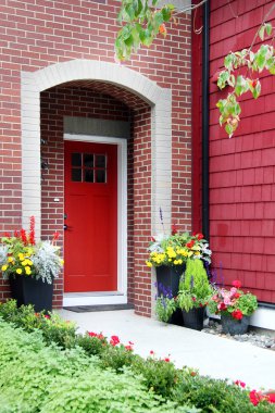 Bir tuğla ev cephesinde çiçekli kırmızı ön kapıdan giriş.