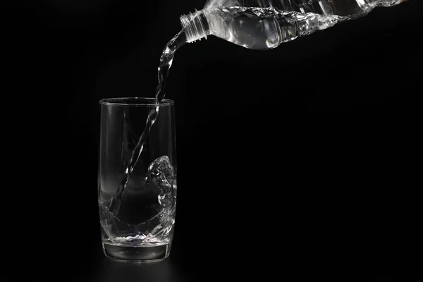 Voda se nalévá z plastové láhve do skla, izolovány na černém pozadí — Stock fotografie