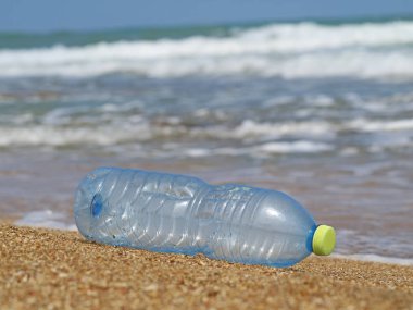 arka planda dalgalar ile sahilde kumda plastik şişe, plastik atık ile deniz kirliliği kavramı