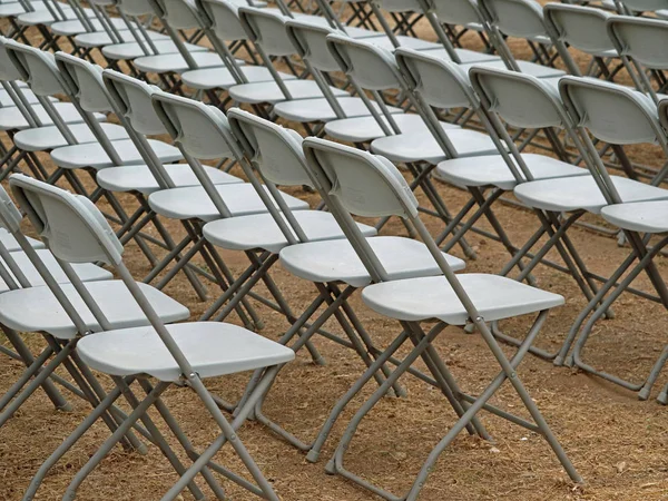 white chairs on sandy ground lined up for a presentation, event, show, conference, lecture, auditorium, or performance.