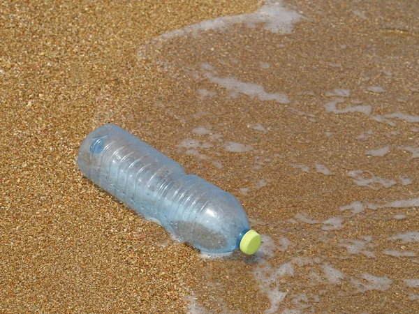 Plastic bottle in the sand on beach with waves in the background, concept of sea pollution with plastic waste — Stock Photo, Image