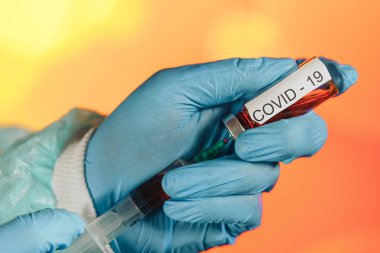 Mavi eldivenli bir sağlık görevlisi şırıngaya ampul çekiyor. Coronavirus gribine karşı tıbbi aşı. Tıbbi cam şişeleri için enjeksiyon şişesi. COVID salgını