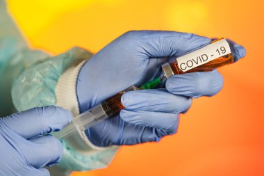 Mavi eldivenli bir sağlık görevlisi şırıngaya ampul çekiyor. Coronavirus gribine karşı tıbbi aşı. Tıbbi cam şişeleri için enjeksiyon şişesi. COVID salgını
