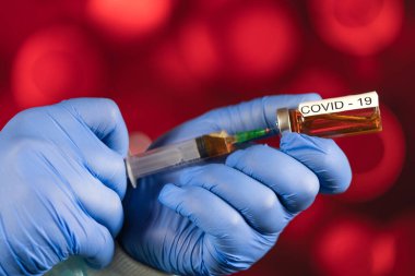 Mavi eldivenli bir sağlık görevlisi şırıngaya ampul çekiyor. Coronavirus gribine karşı tıbbi aşı. Tıbbi cam şişeleri için enjeksiyon şişesi. COVID salgını