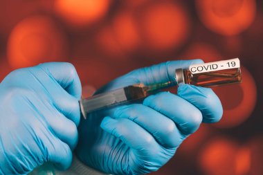 Mavi eldivenli bir sağlık görevlisi şırıngaya ampul çekiyor. Coronavirus gribine karşı tıbbi aşı. Tıbbi cam şişeleri için enjeksiyon şişesi. COVID salgını