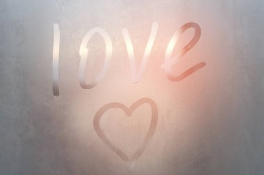 Terli bardağa kazınmış aşk ve kalp. Renkli arka planda sisli cam bir pencereye çizilmiş aşk kalbi. Sisli camda aşkın ve mutluluğun sembolü.