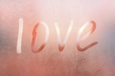 Terli bardaktaki yazıt aşkı. Renkli arka planda sisli cam bir pencereye çizilmiş aşk. Sisli camda aşkın ve mutluluğun sembolü.