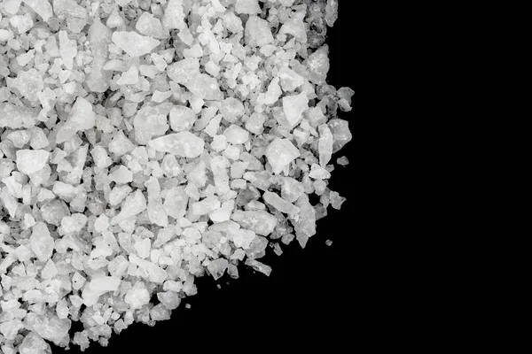 Spilled white sea salt isolated black background. Clear crystalline shaker pebbles on a black background, macro, close up