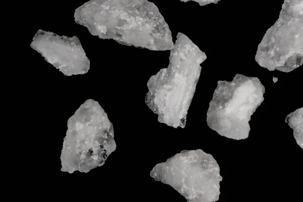 Spilled white sea salt isolated black background. Clear crystalline shaker pebbles on a black background, macro, close up