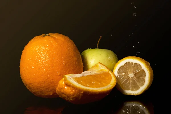 Apples and oranges fruits with drops and splashes of water on a black background