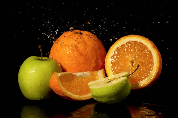 Apples and oranges fruits with drops and splashes of water on a black background