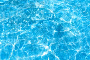  Sahilin arka planında mavi şeffaf deniz suyu. Güneşli bir günde hafif dalgalar ve parlayan temiz su yüzeyi. deniz tatili