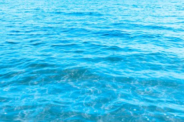 Sahilin arka planında mavi şeffaf deniz suyu. Güneşli bir günde hafif dalgalar ve parlayan temiz su yüzeyi. deniz tatili