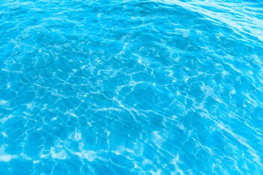  Sahilin arka planında mavi şeffaf deniz suyu. Güneşli bir günde hafif dalgalar ve parlayan temiz su yüzeyi. deniz tatili