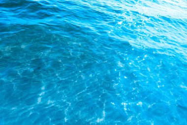  Sahilin arka planında mavi şeffaf deniz suyu. Güneşli bir günde hafif dalgalar ve parlayan temiz su yüzeyi. deniz tatili