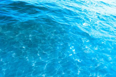  Sahilin arka planında mavi şeffaf deniz suyu. Güneşli bir günde hafif dalgalar ve parlayan temiz su yüzeyi. deniz tatili