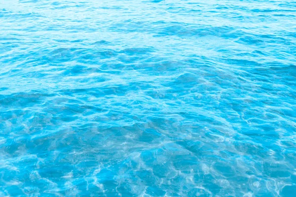ビーチのテクスチャの背景の近くの青い透明な海の水 晴れた日にわずかな波とグレアで澄んだ水の表面 海の休暇 — ストック写真