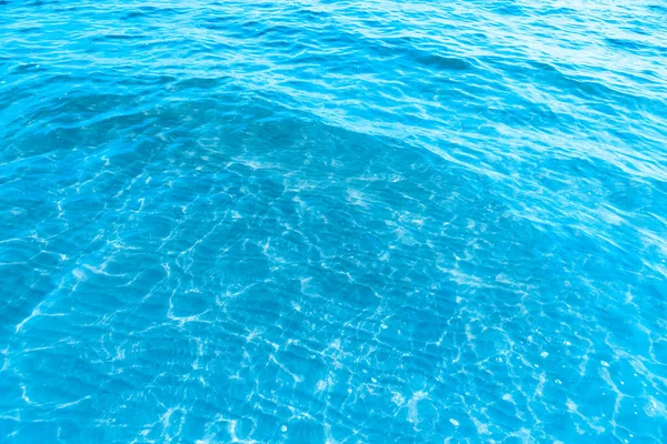 ビーチのテクスチャの背景の近くの青い透明な海の水 晴れた日にわずかな波とグレアで澄んだ水の表面 海の休暇 — ストック写真