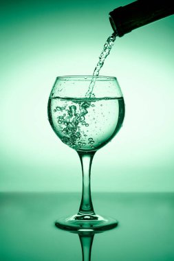 Yeşil bir arkaplanda akan suyla (beyaz şarap) şarap kadehi