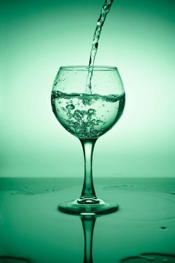 Yeşil bir arkaplanda akan suyla (beyaz şarap) şarap kadehi