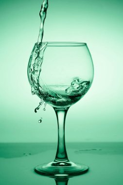 Yeşil bir arkaplanda akan suyla (beyaz şarap) şarap kadehi