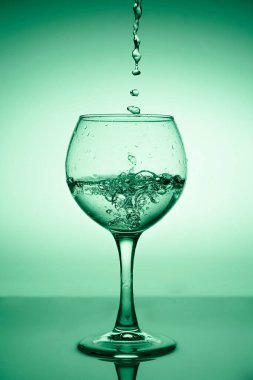 Yeşil bir arkaplanda akan suyla (beyaz şarap) şarap kadehi