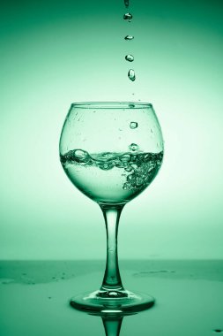 Yeşil bir arkaplanda akan suyla (beyaz şarap) şarap kadehi