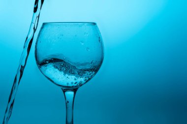 Mavi zemin üzerinde sıvı (beyaz şarap) olan şarap kadehi