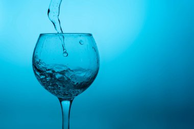 Mavi zemin üzerinde sıvı (beyaz şarap) olan şarap kadehi