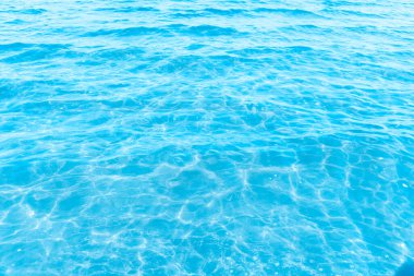 Sahilin arka planında mavi şeffaf deniz suyu. Güneşli bir günde hafif dalgalar ve parıltılarla berrak su yüzeyi