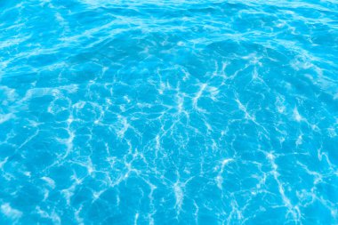 Sahilin arka planında mavi şeffaf deniz suyu. Güneşli bir günde hafif dalgalar ve parıltılarla berrak su yüzeyi