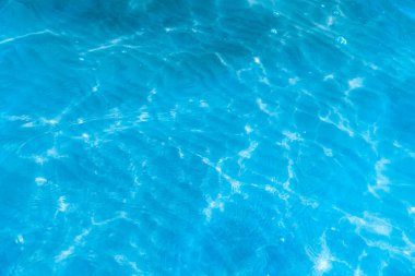 Sahilin arka planında mavi şeffaf deniz suyu. Güneşli bir günde hafif dalgalar ve parıltılarla berrak su yüzeyi