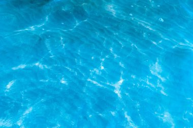 Sahilin arka planında mavi şeffaf deniz suyu. Güneşli bir günde hafif dalgalar ve parıltılarla berrak su yüzeyi